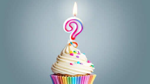 Cupcake in a rainbow coloured cup, with coloured sprinkles and a lit question mark candle on top - created by Ask An Iranian